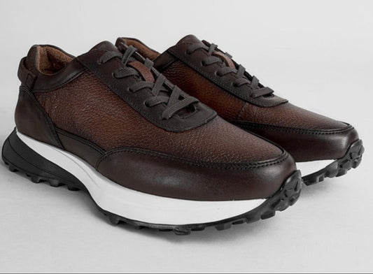 A pair of men's low-top sneakers in dark brown textured leather with black laces, a thick white midsole, and a black rugged outsole, shown on a light gray background.